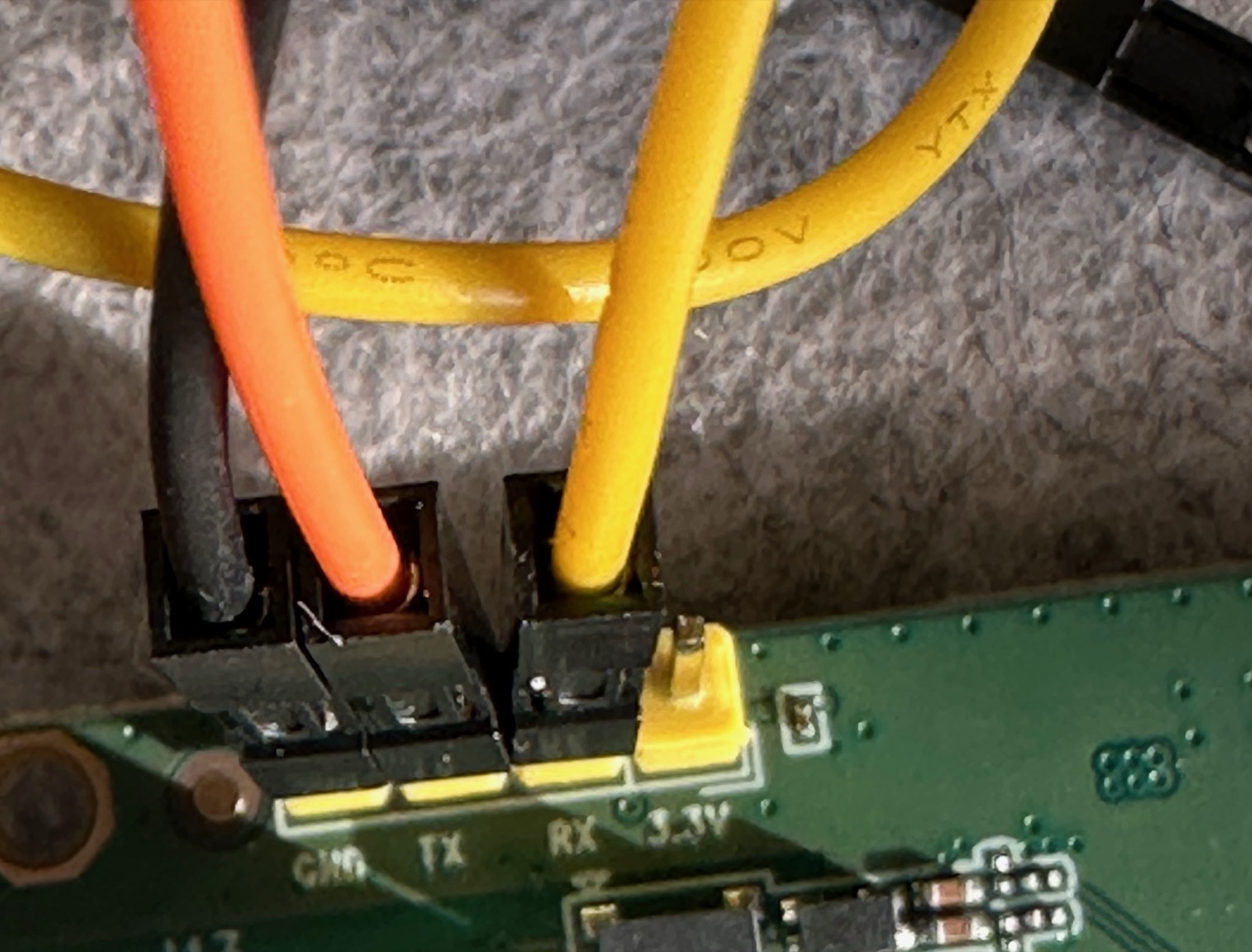Router-side UART wiring on the Brume 2 with black, orange, and yellow jumper wires connected near the GND, TX, RX, and 3V3 silkscreen